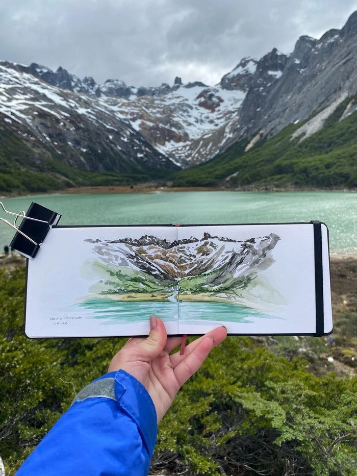 Sketchbook con la Laguna Esmeralda en acuarela, sostenido frente a la laguna turquesa y las montañas nevadas